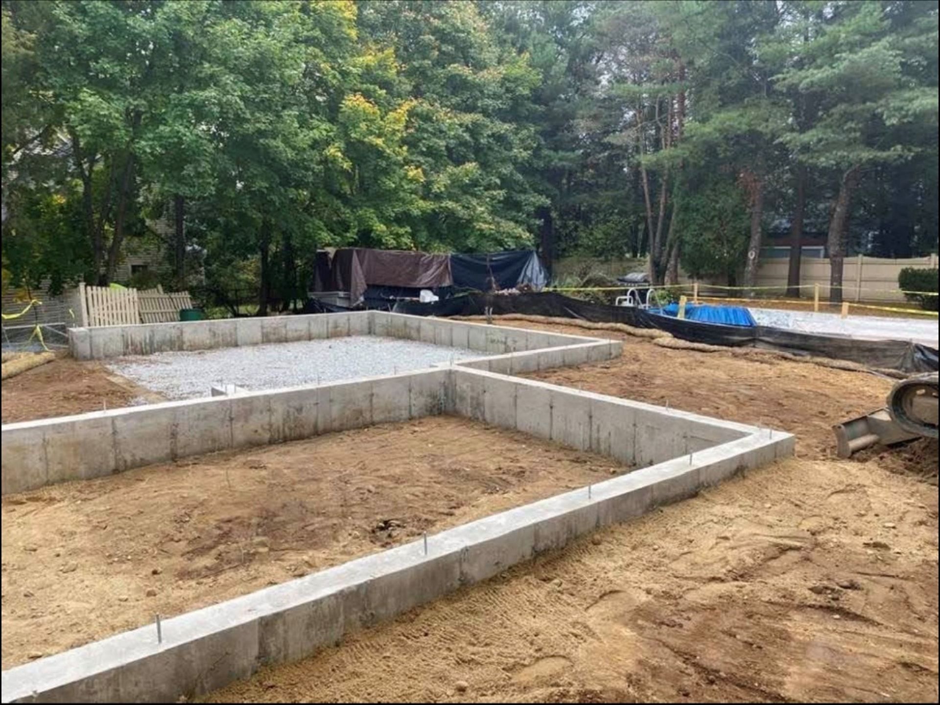 Foundation footings being built on a cleared dirt lot, with trees and construction materials nearby