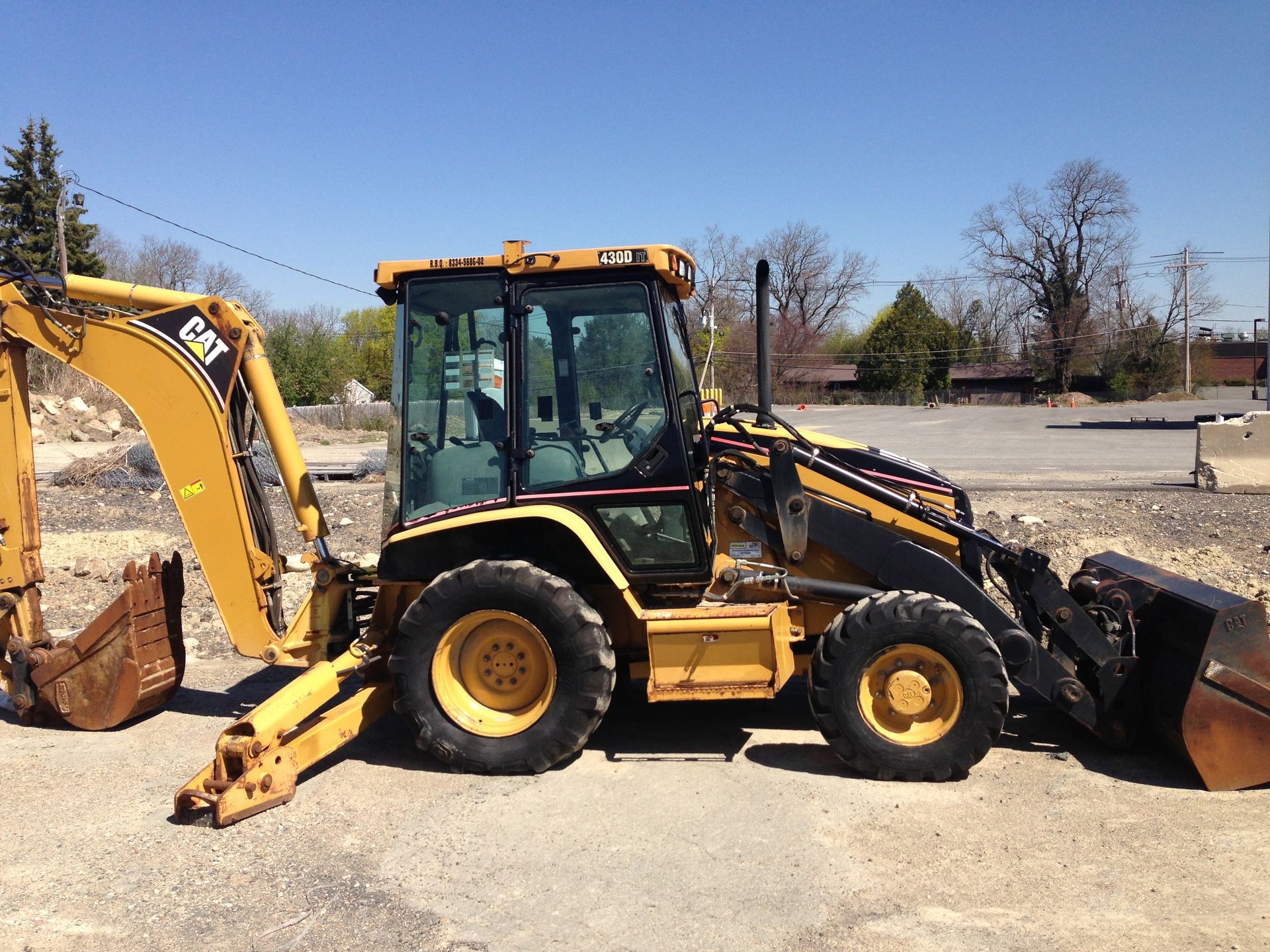 Yellow backhoe loader parked on a gravel lot with a bucket lowered in front