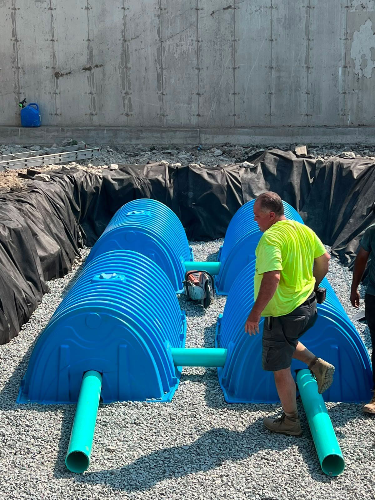 Worker beside blue pipe and gravel-lined trench at a construction site