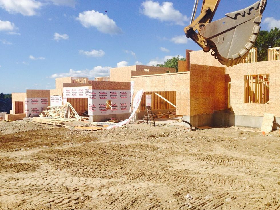 Construction site with brick walls under construction and an excavator bucket lifting debris on a dusty lot.