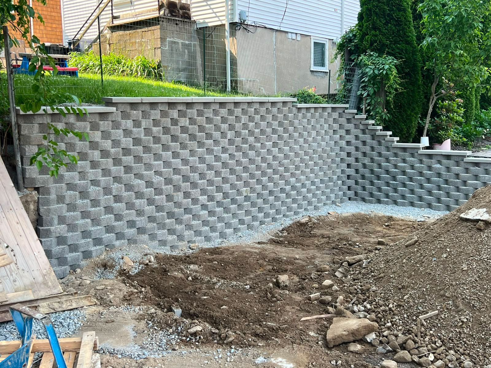 Backyard under construction with a gray retaining wall and dirt pile in front