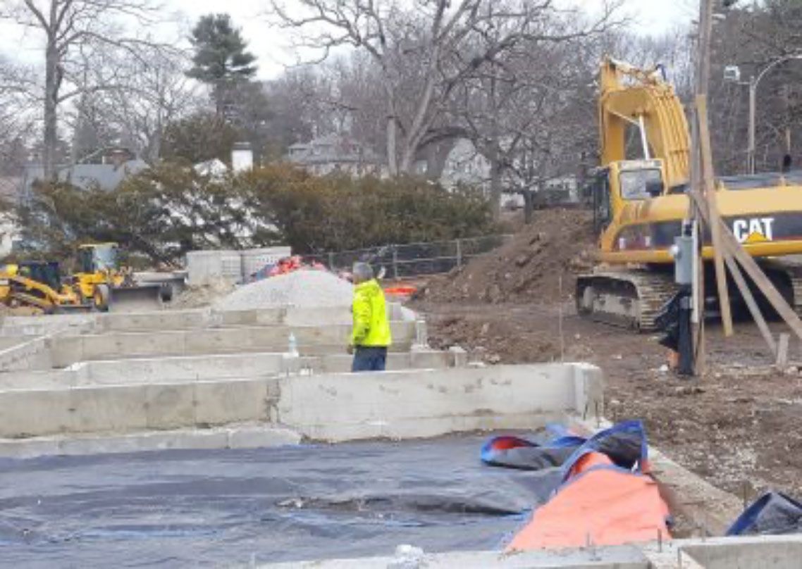 Construction site with excavator, concrete retaining walls, and a worker in a neon jacket
