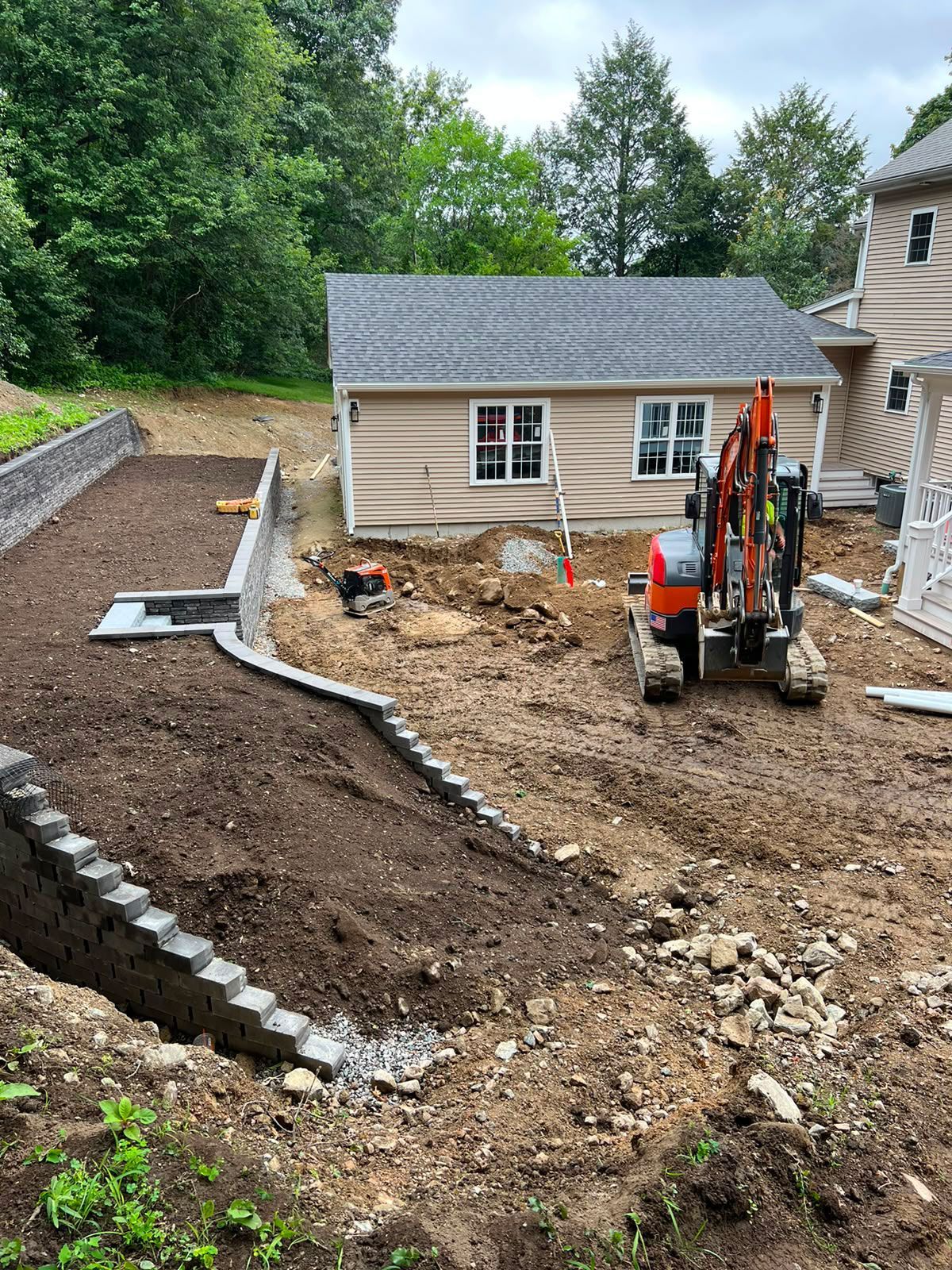 Backyard excavation with mini excavator, gravel path, and a house under construction