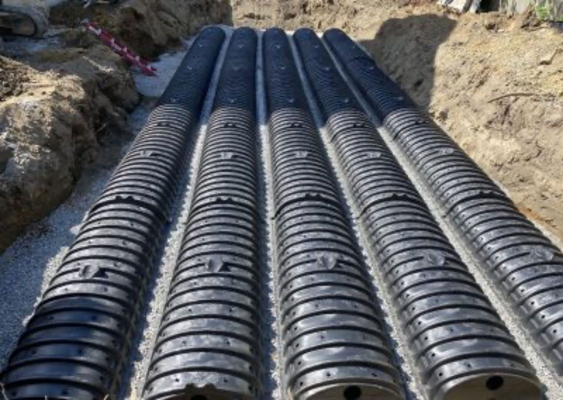 Rows of black corrugated plastic pipes laid on a dirt construction site