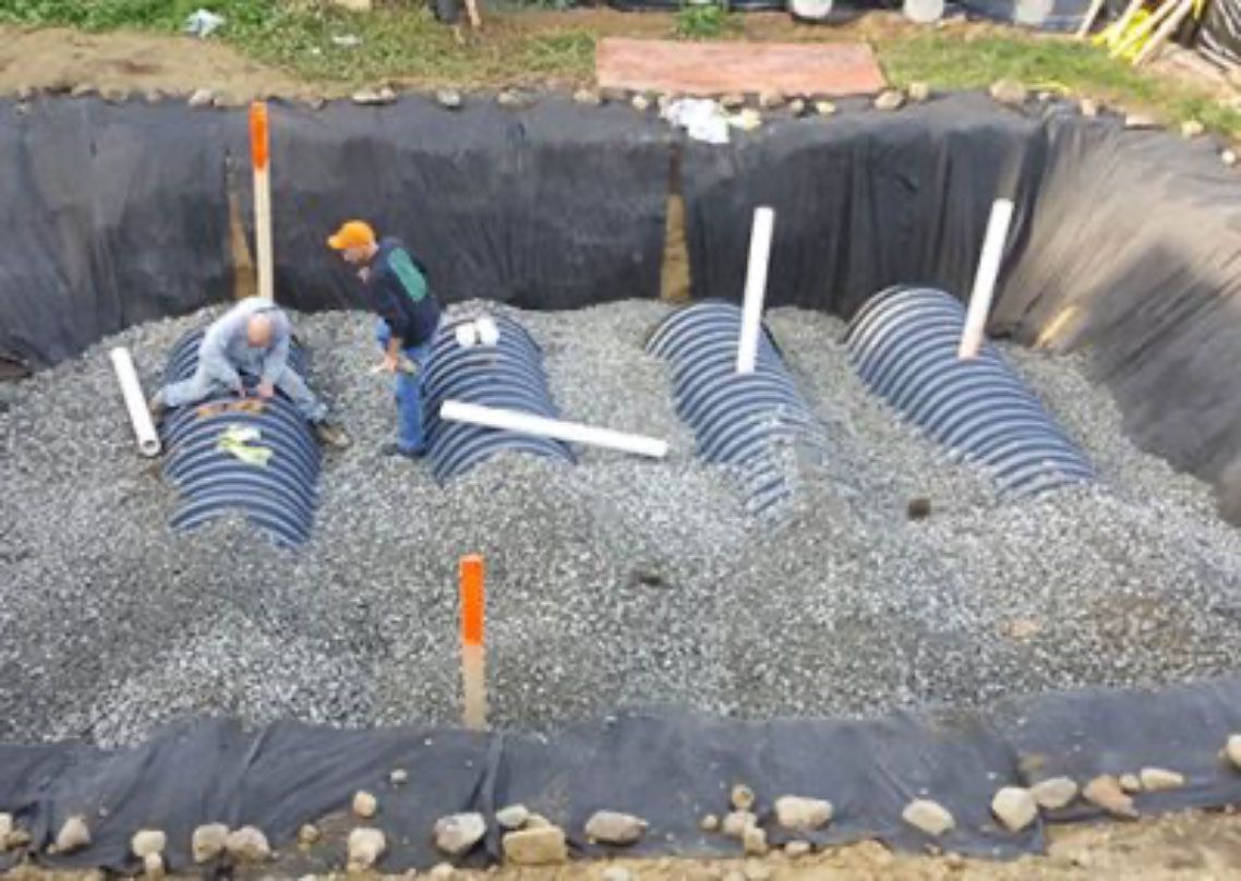 Workers installing corrugated drainage pipes in a gravel-lined excavation site