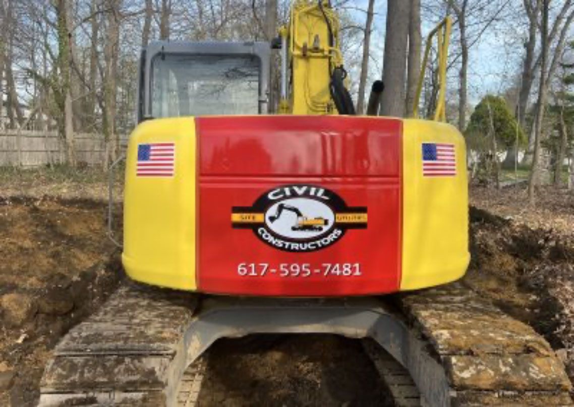 Red and yellow civil excavation machine with U.S. flags and phone number in a wooded worksite