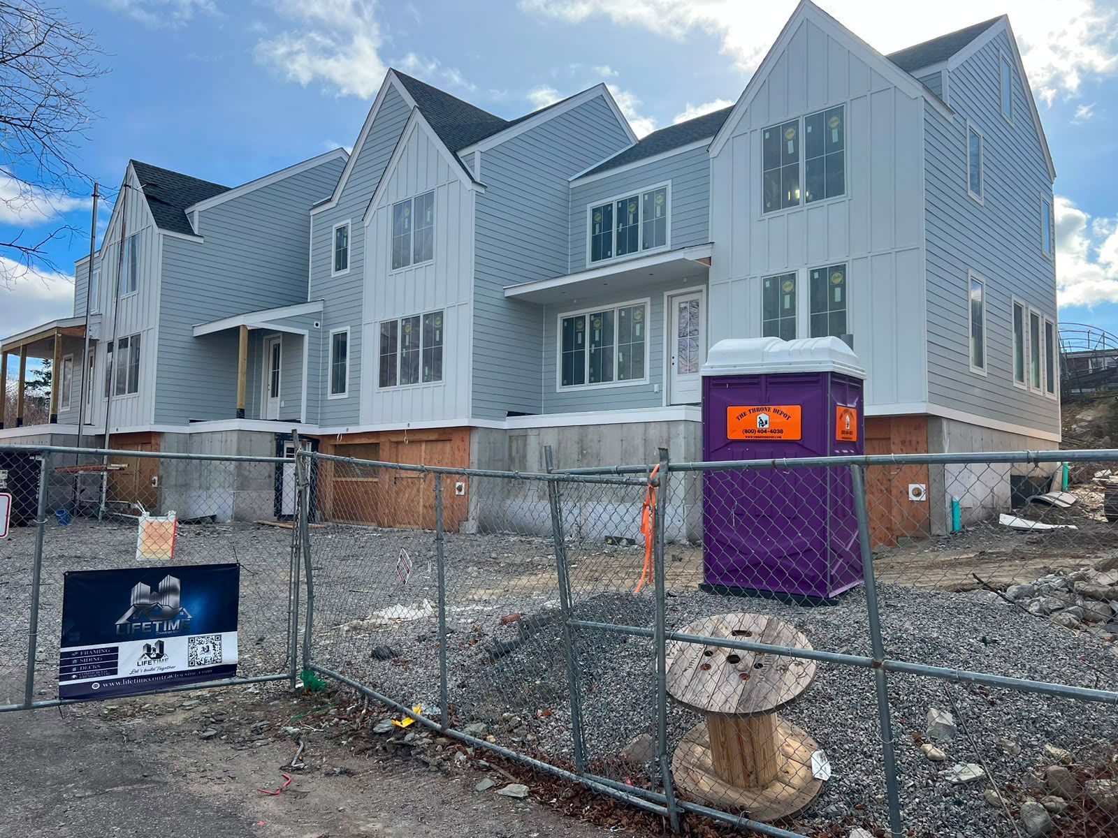New row of gray townhouses behind chain-link fencing, with a purple portable toilet in front