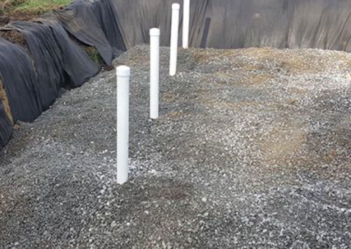 White drainage pipes stand in a gravel pit beside dark tarps and rock walls.