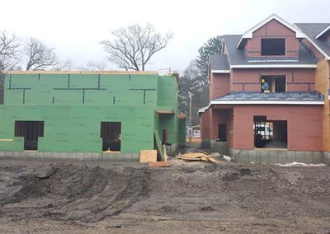 Partially built house with green and red exterior walls at a muddy construction site
