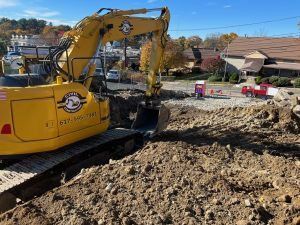 Yellow excavator working on a muddy construction site with dirt piles and houses in the background