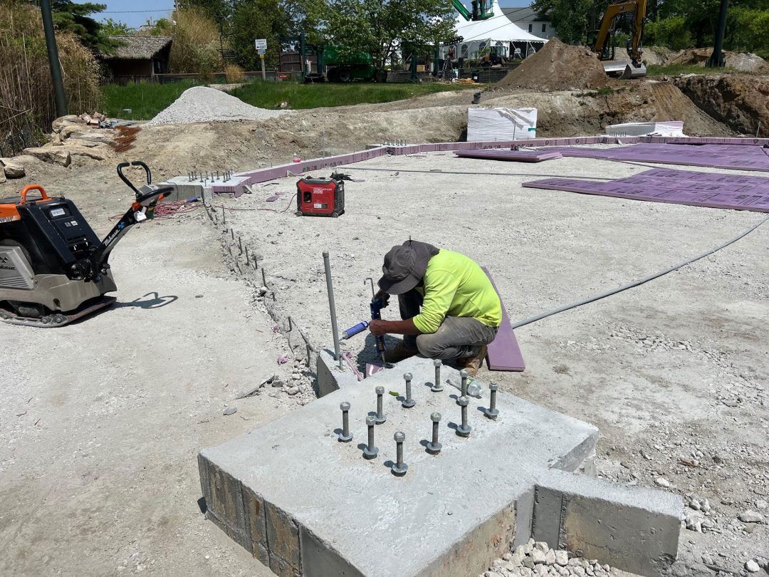 Worker drilling anchor bolts into a concrete foundation at a construction site
