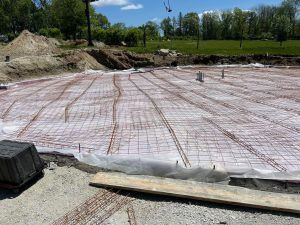 Construction site with rebar mesh and plastic sheeting laid over a large excavated foundation area