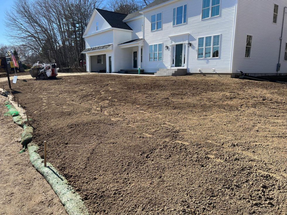 Newly graded dirt yard beside a white two-story house on a sunny day