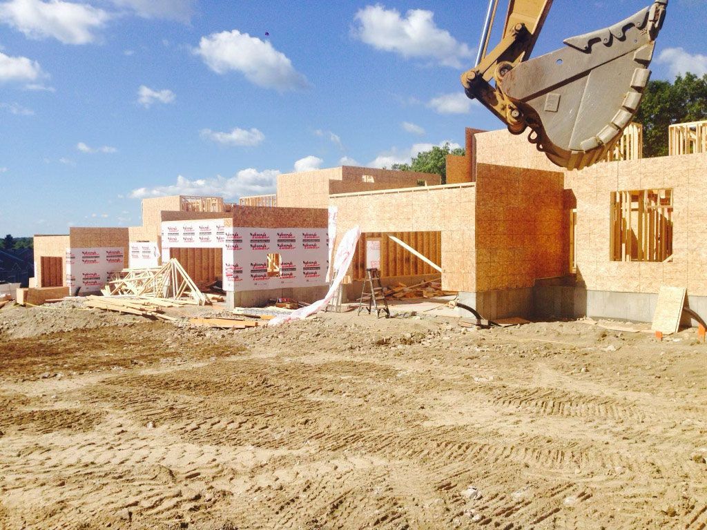 Construction site with excavator bucket above unfinished brick building under a blue sky