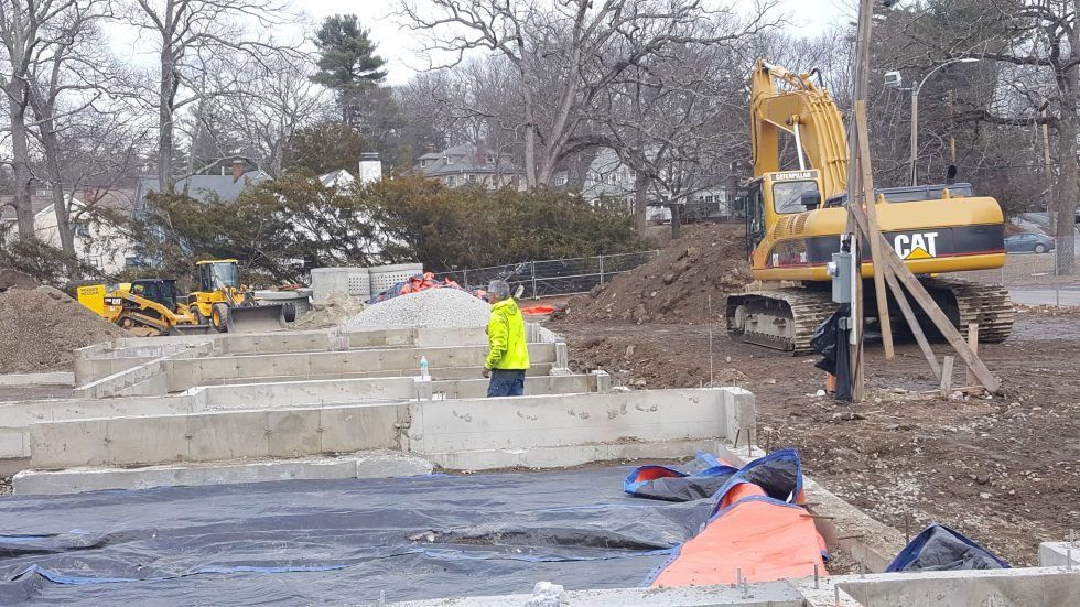Construction site with excavators, concrete blocks, and workers in high-visibility gear near a road