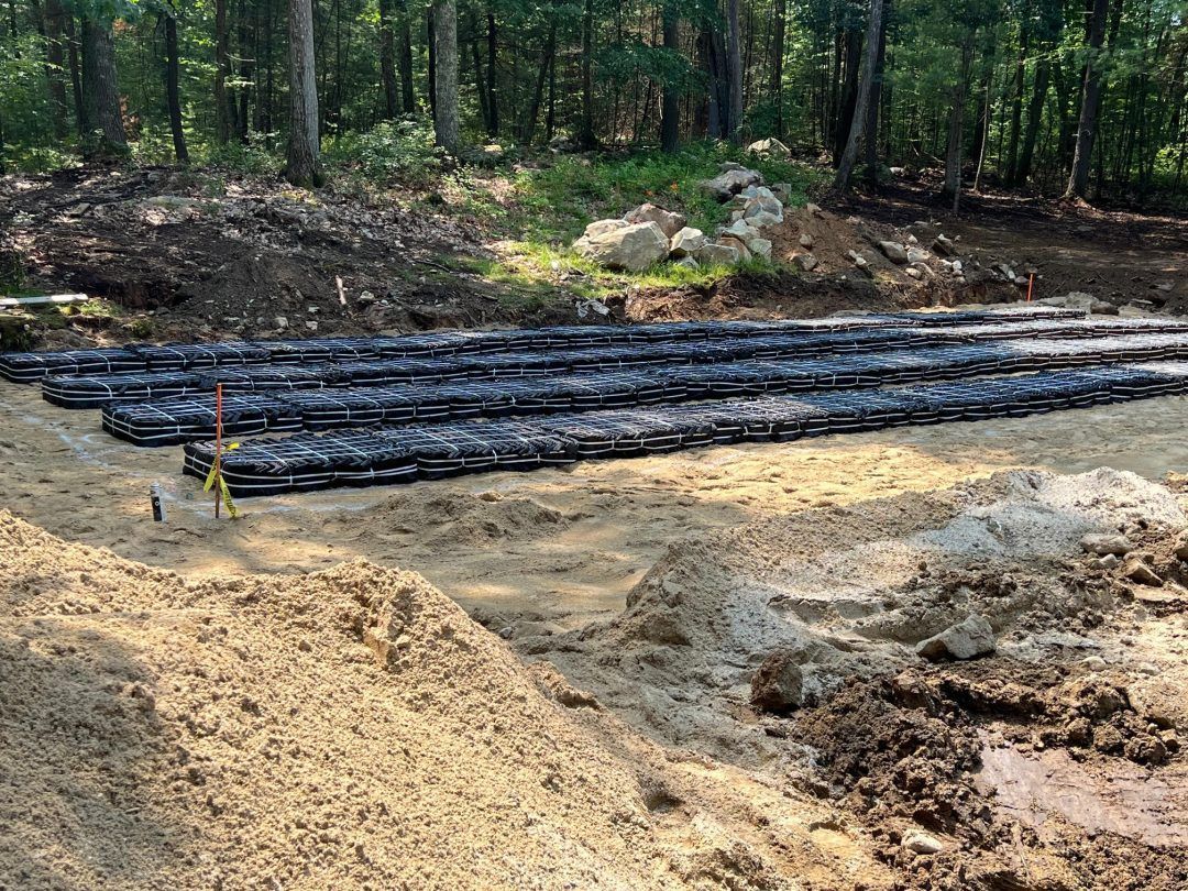 Construction site with black erosion-control logs on a dirt clearing beside a wooded area.