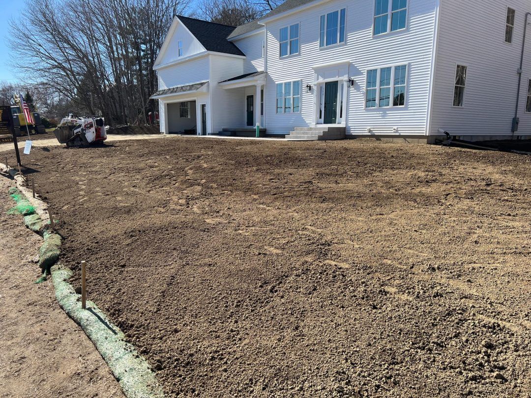 Freshly graded front yard beside a white house with blue shutters and a mulch border