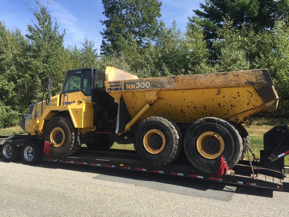 Yellow dump truck loaded on a flatbed trailer parked outdoors beside trees and grass