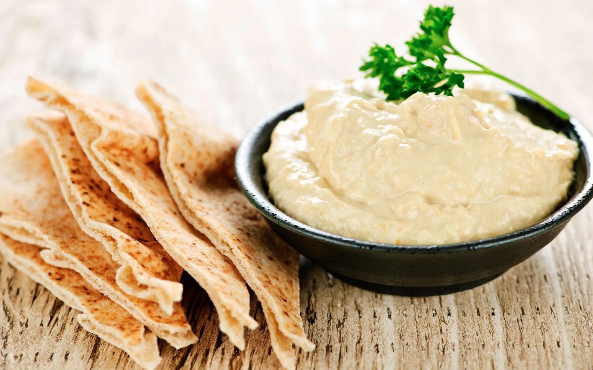 a bowl of hummus next to a stack of pita bread on a wooden table