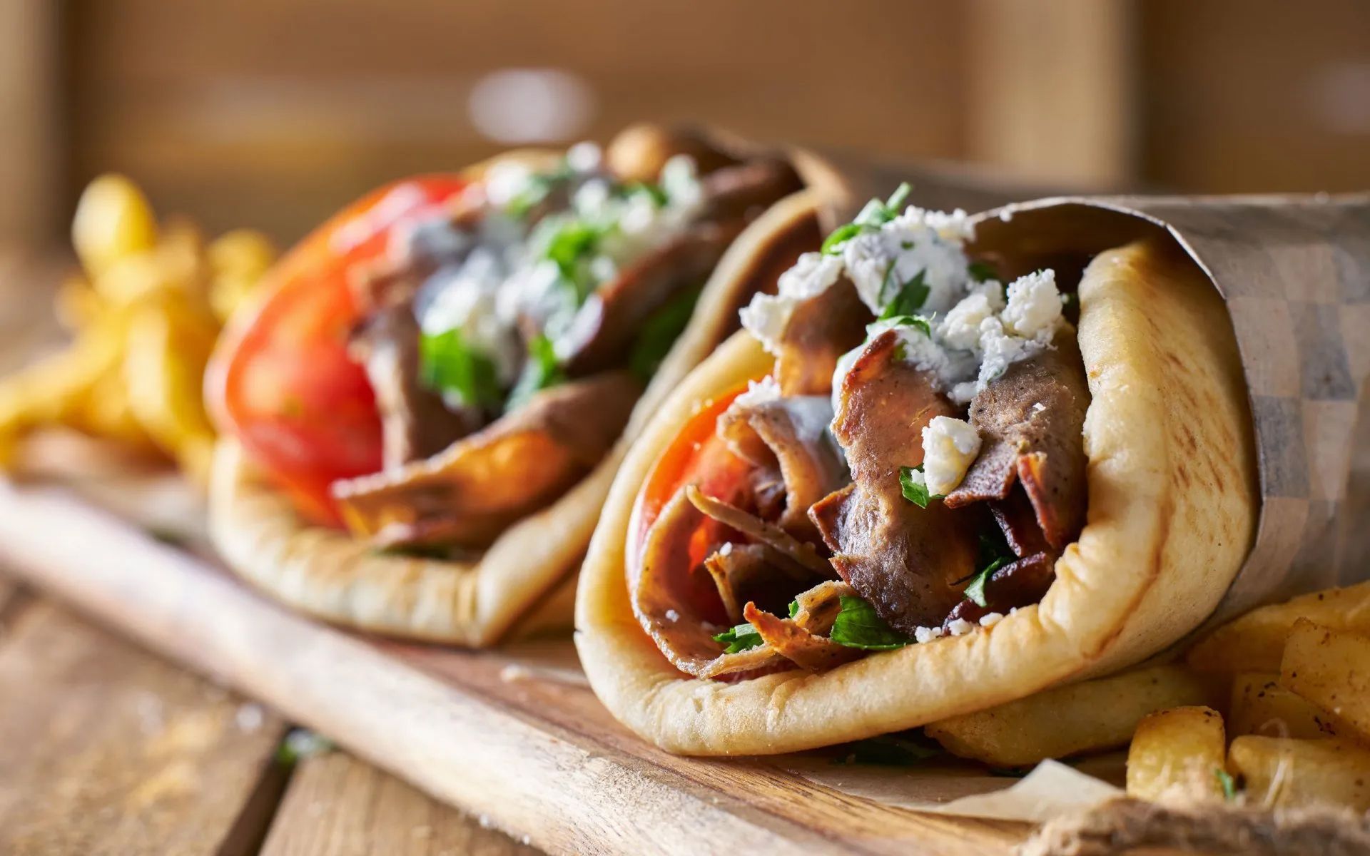 two gyros and french fries on a wooden cutting board
