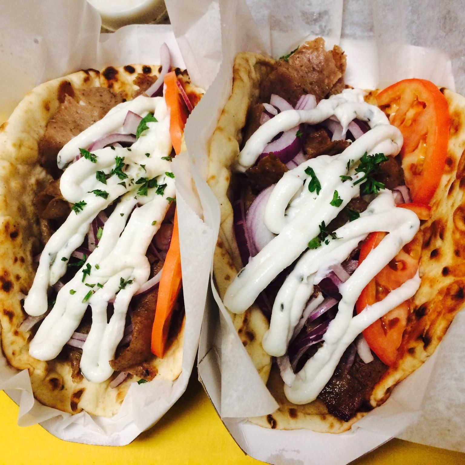 two gyros with onions tomatoes and white sauce on them