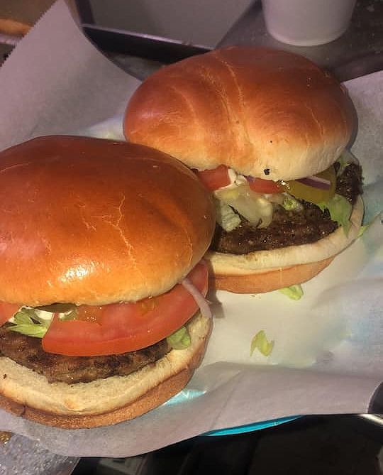 two hamburgers with lettuce, tomato, and onions on a plate