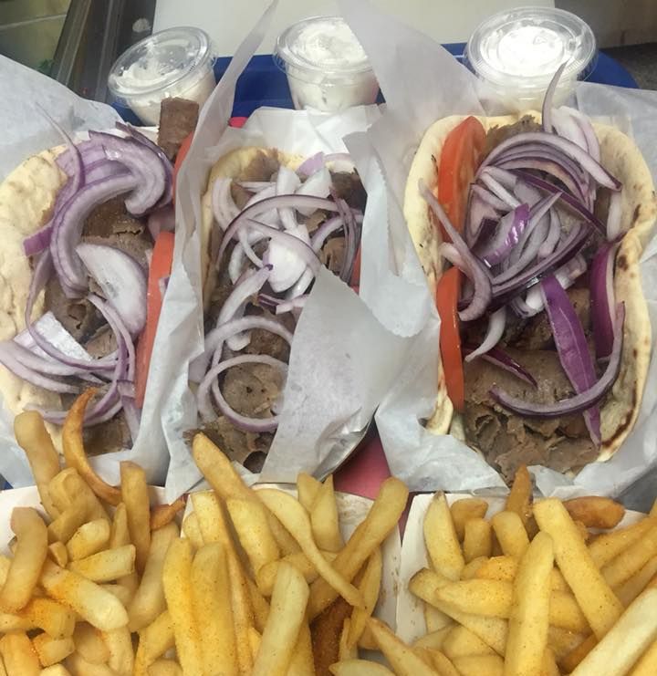 three gyros with onions and french fries on a tray