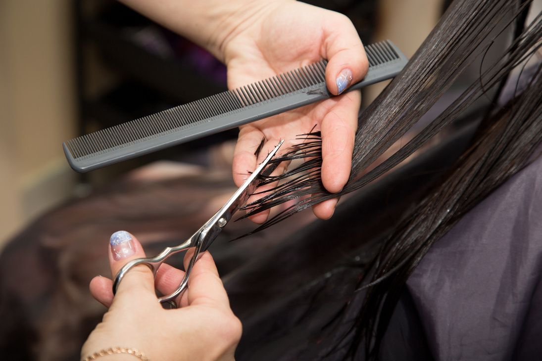 Hands holding comb and scissors, cutting dark hair in salon.