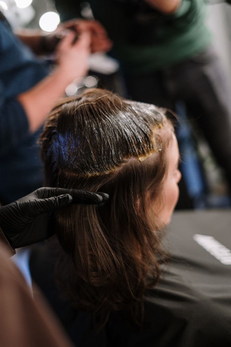 Hairdresser applying hair dye to a client's hair in a salon. Black gloves, brown hair.