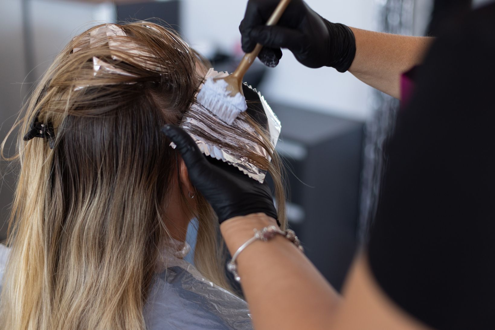 Hairdresser applying hair dye with brush. Blonde hair in foils. Black gloves.