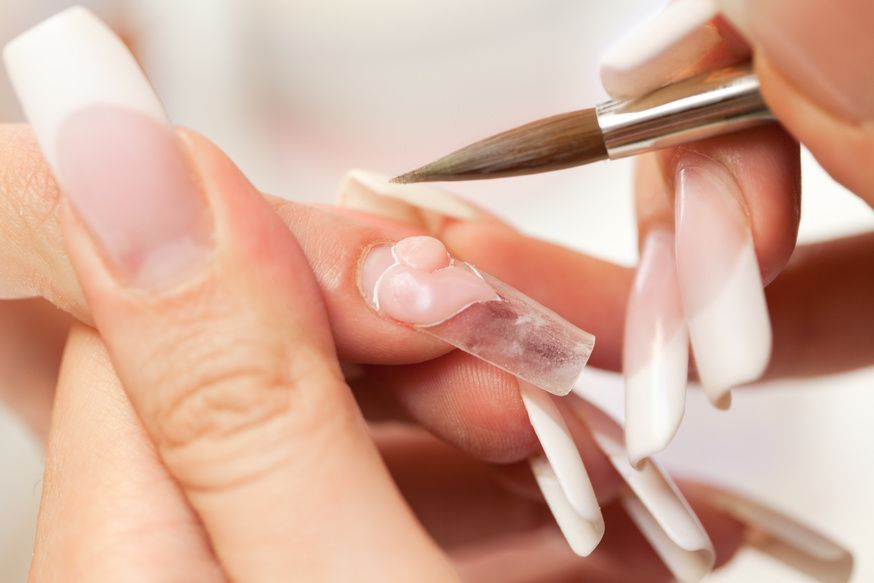 Person applying acrylic nail with brush to a long, French tip nail.