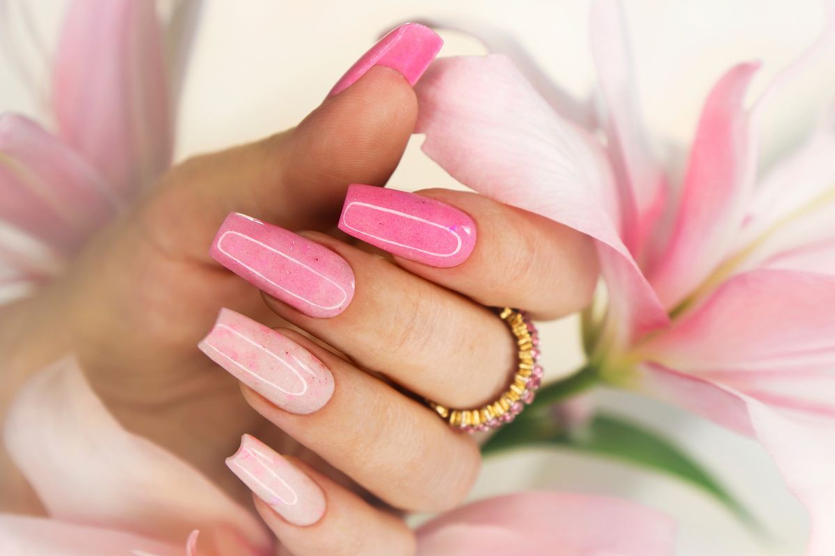 Hand with long, pink acrylic nails, a gold ring, and lily petals.