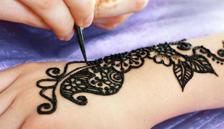 Hand being decorated with black henna design using a cone applicator.