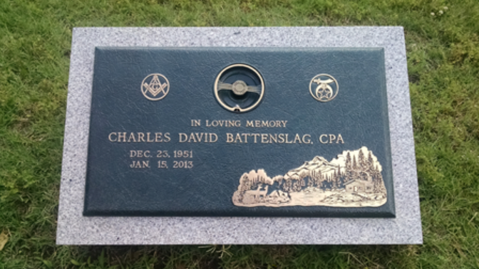 A bronze and stone headstone for Charles David Battenslag, featuring Masonic symbols, a steering wheel, and a mountain.