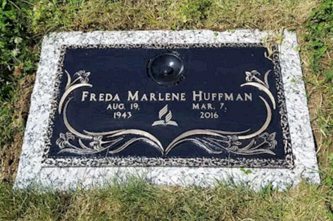 A granite headstone for Freda Marlene Huffman (1943–2016), featuring decorative floral etchings on a black slab.