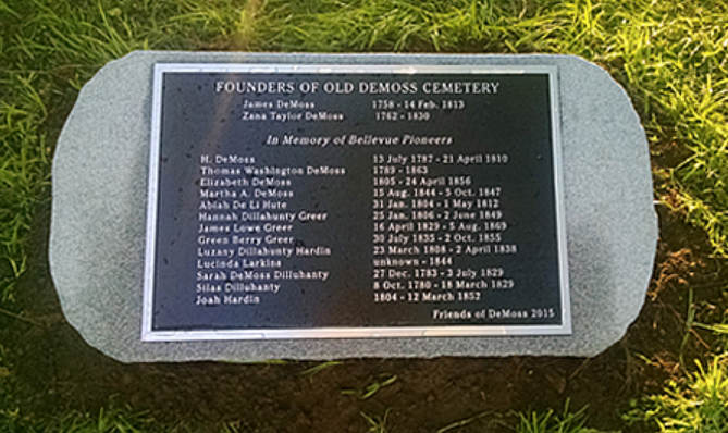 A stone plaque in a grassy area lists the names and dates of the Founders of Old DeMoss Cemetery and Bellevue pioneers.