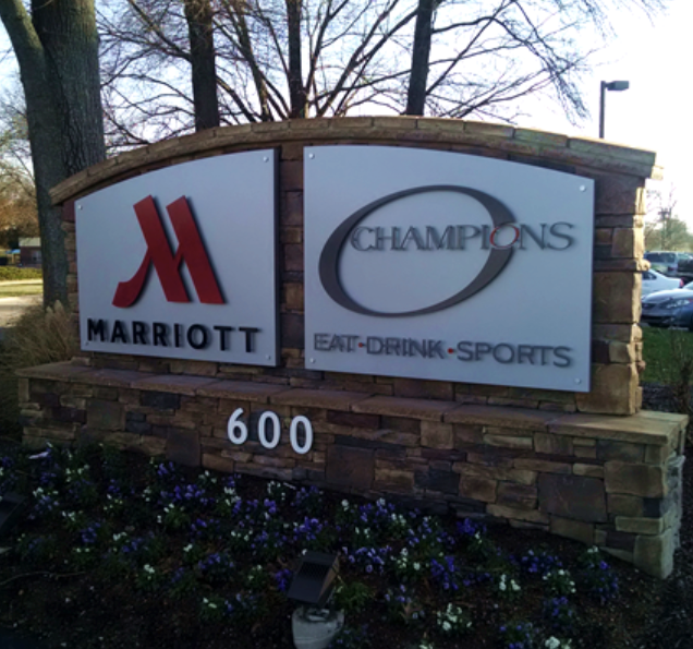 A stone monument sign for a Marriott hotel and Champions restaurant, featuring the address 600, surrounded by flowers.