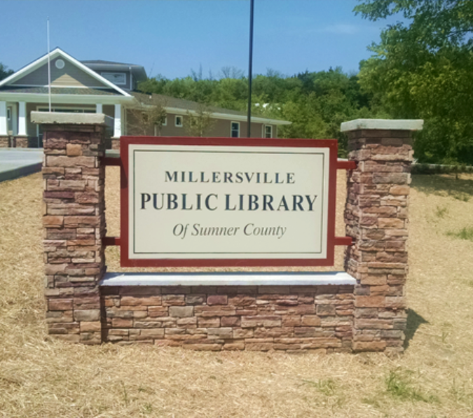 A stone monument sign for the Millersville Public Library of Sumner County, set against a lawn and library building.