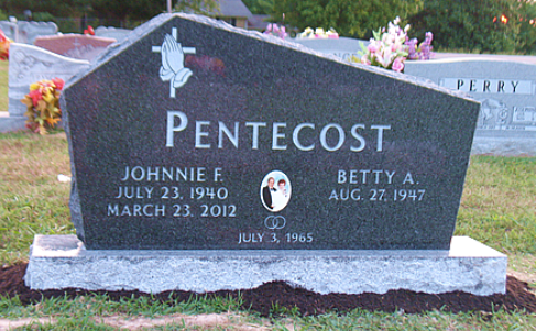 A dark granite headstone for Johnnie F. and Betty A. Pentecost, featuring a cross and praying hands, in a cemetery.