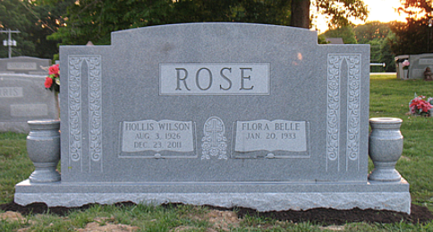 A grey granite double headstone for the Rose family in a cemetery, featuring engraved names, dates, and decorative vases.
