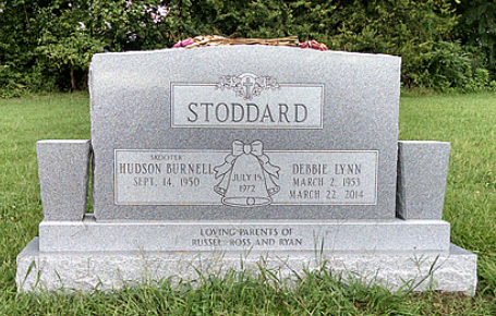 A grey granite Stoddard family headstone in a grassy field, inscribed with the names Hudson Burnell and Debbie Lynn.