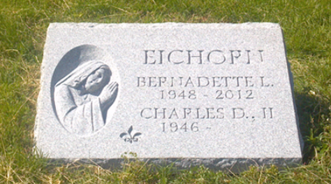 A gray granite headstone for Bernadette L. (1948–2012) and Charles D. II (1946–) Eichoff with a bas-relief of a praying figure.