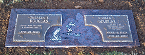 A dark granite double headstone for Theresa F. and Ronald E. Douglas, featuring an etched scene of a person fishing.