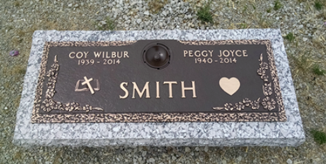 A bronze grave marker for Coy Wilbur and Peggy Joyce Smith, dated 1939-2014 and 1940-2014, set on a granite base.