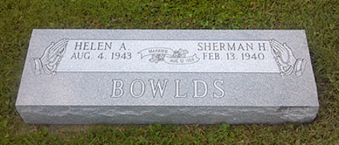 A gray granite grave marker for the Bowlds family, inscribed with names Helen A. and Sherman H., set in grass.