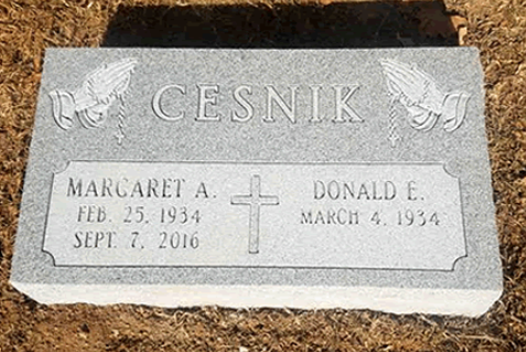 A gray granite headstone for Margaret A. and Donald E. Cesnik, with carved praying hands and a central cross.