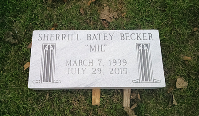 A light gray rectangular gravestone sits in grass, inscribed with 