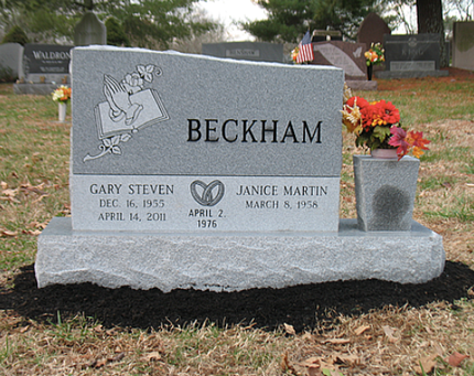A gray granite gravestone for the Beckham family with praying hands, a wedding date, and flower arrangements.