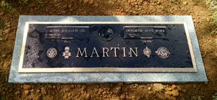 A flat, rectangular bronze memorial plaque on a granite base, engraved with the name 