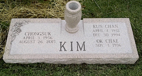 A granite cemetery headstone with a central vase, engraved with the surname 